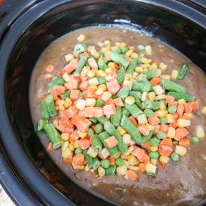 Close up view of process shot- adding frozen veggies into the crock pot.