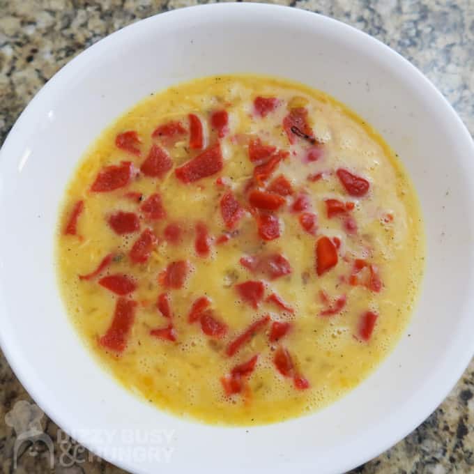Overhead view of roasted red peppers and beaten eggs combined in a white bowl