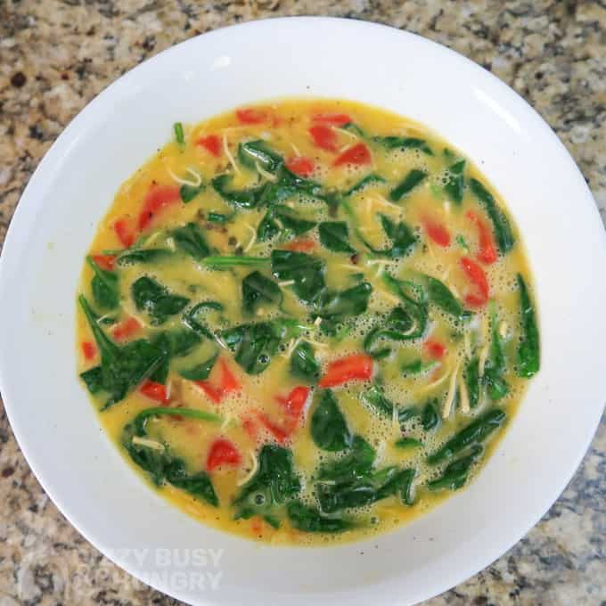 Overhead view of spinach and cheese added to the roasted red pepper and egg mixture