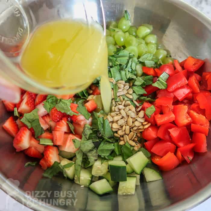 Process shot of dressing being poured into the bowl of chopped fruits and veggies.