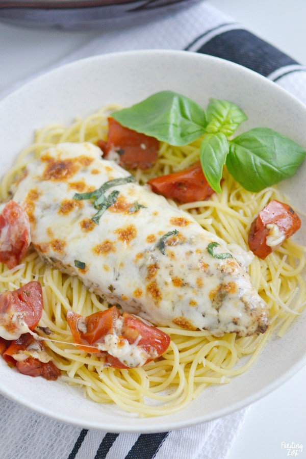 Top view of Baked Chicken Caprese over cooked spaghetti on a white plate