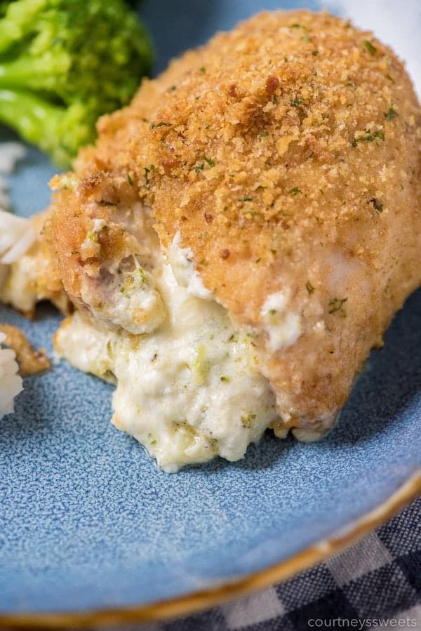 Front view of chicken thigh crusted with bread crumbs. Cheese and broccoli stuffing coming out of it