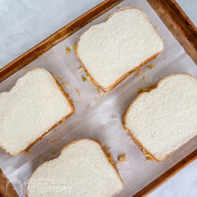 Overhead view of 4 Parmesan and butter coated sandwiches on a baking sheet ready for the oven