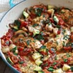 Top view of cooked chicken mixed with zucchini, mushrooms in a blue cast iron pan - cheap chicken recipes