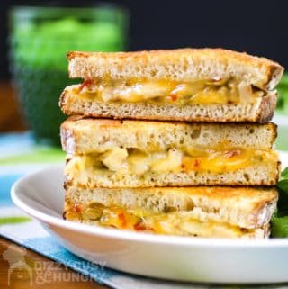 Three halves of a grilled chicken sandwich with cheese stacked on a white plate.