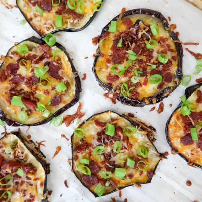 Process shot of eggplant rounds still on baking sheet with parchment paper topped with cheese, bacon, and chopped scallions.