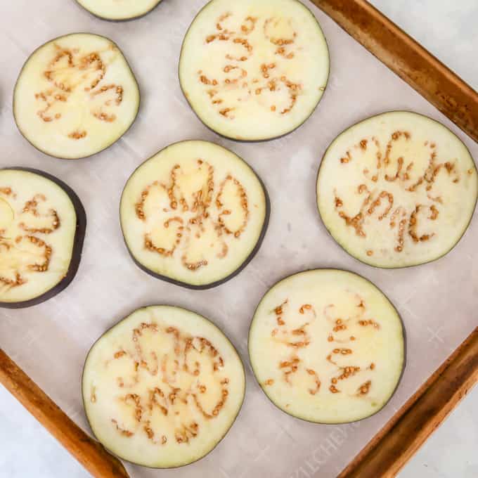Overhead shot of eight eggplant discs on a baking sheet with parchment paper.