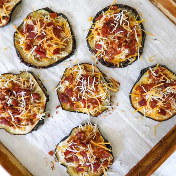 Process shot of crisped eggplant discs topped with cheese and bacon pieces.