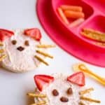 Angle view of a bagel with cream cheese with pretzel rods, strawberries and raisins shaped as a cat face
