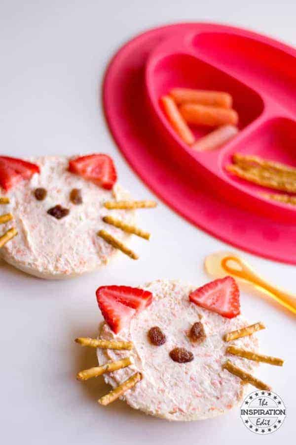 Angle view of a bagel with cream cheese with pretzel rods, strawberries and raisins shaped as a cat face