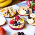 angle view of apple slices topped with fruits, peanut butter and nuts - after school snacks