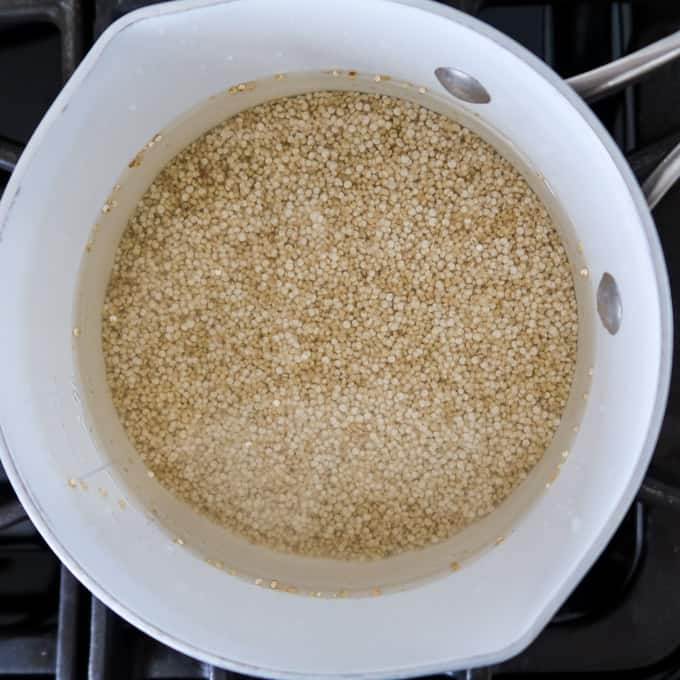 Overhead shot of white pot on stove filled with quinoa and water cooking.