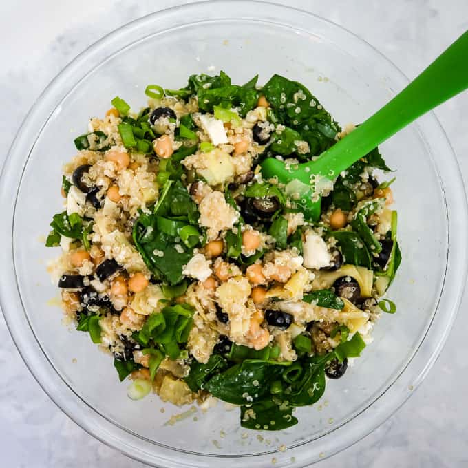 Previous mixture combined with feta crumbles, chopped scallions, and spinach in a clear bowl with a green spatula.