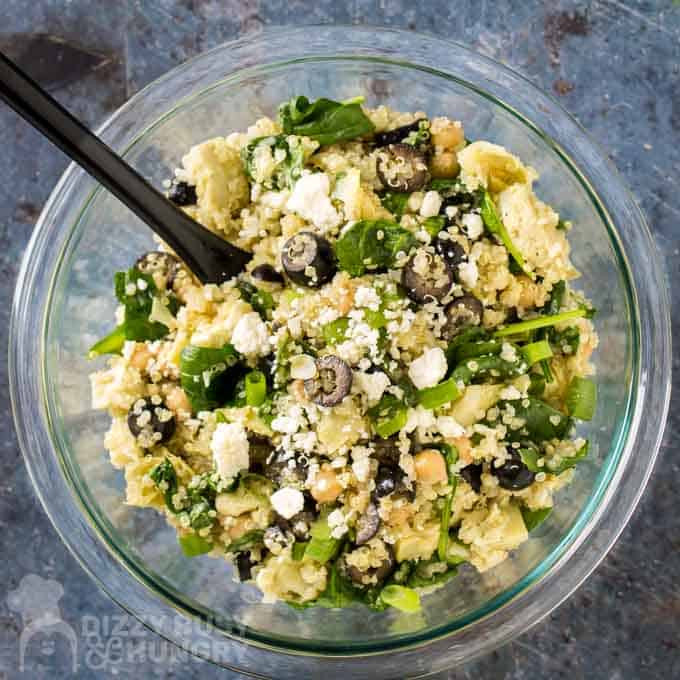 Finished overhead shot of Quinoa Chickpea Salad in a clear bowl on a grey surface with black spoon.