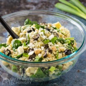 Side view of finished Quinoa Chickpea Salad in a clear bowl with a black spoon in front of scallions.