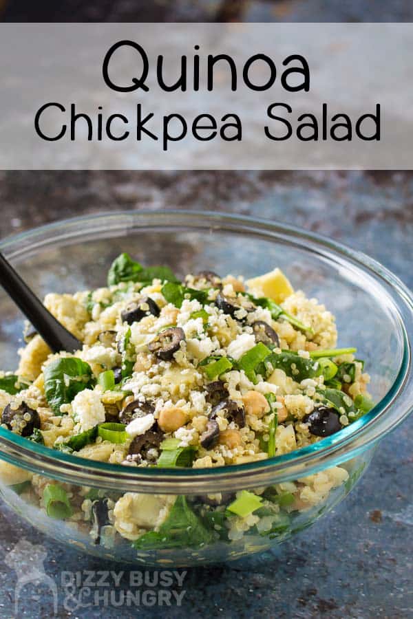 Side close up view of finished Quinoa Chickpea Salad in a clear bowl with a black spoon and a grey background.