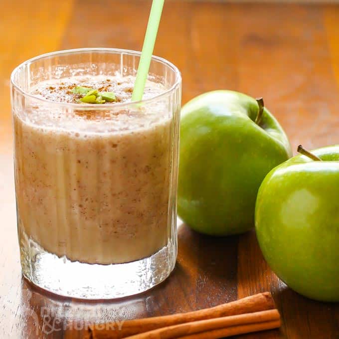 Side view of smoothie with cinnamon and crushed apples on top with a green straw.