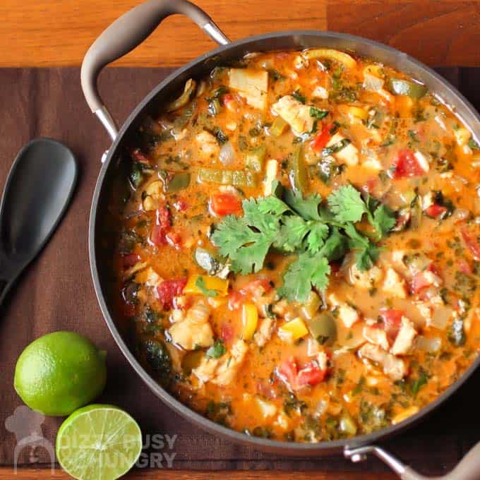 Close up view of fish stew with a cilantro garnish with halved limes and a black spoon.