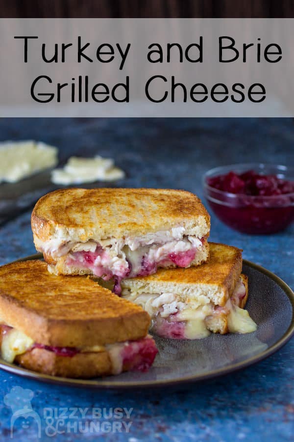 Side view of three stacked halves of brie grilled cheese with cranberry sauce and sliced cheese on a blue background.