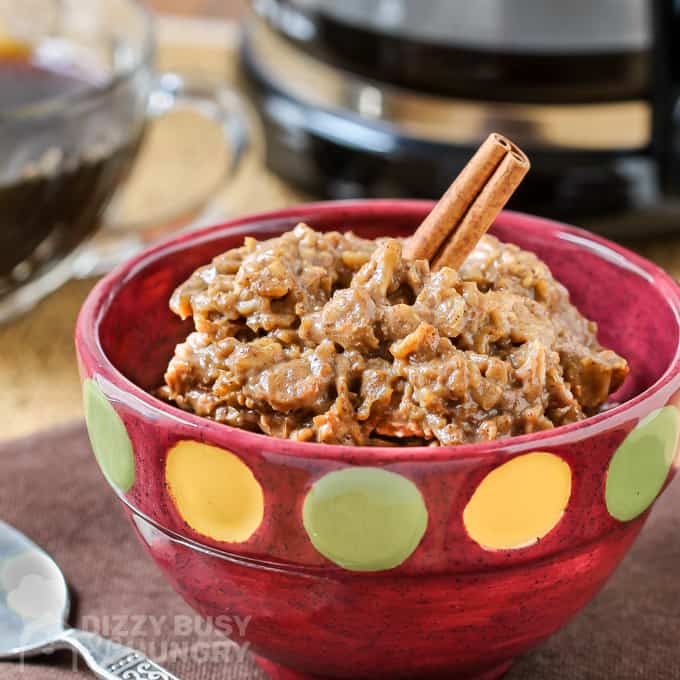 Side view of oatmeal in a red bowl with two cinnamon sticks on top.
