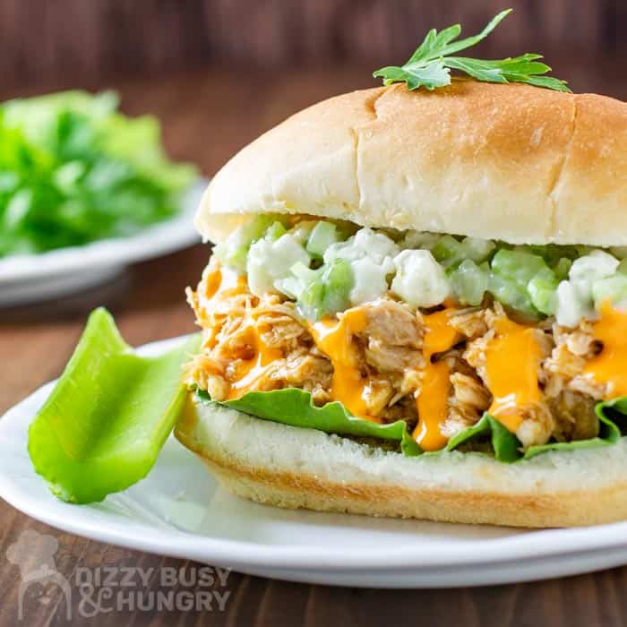 Side view of buffalo chicken sandwich with a side of celery on a white plate and wooden background.