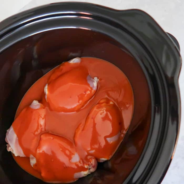 Close up shot of chicken covered with buffalo chicken sauce in a black crock pot.