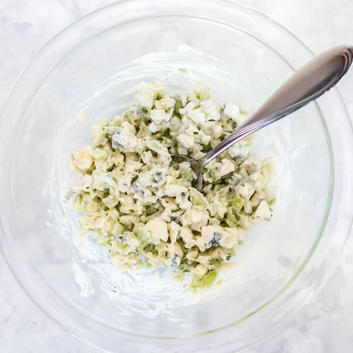 Overhead shot of celery and blue cheese relish mixed with silver spoon in a clear bowl.