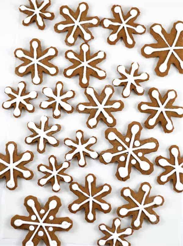 Top view of gingerbread cookies shaped like snowflakes and topped with white icing on a white surface. 