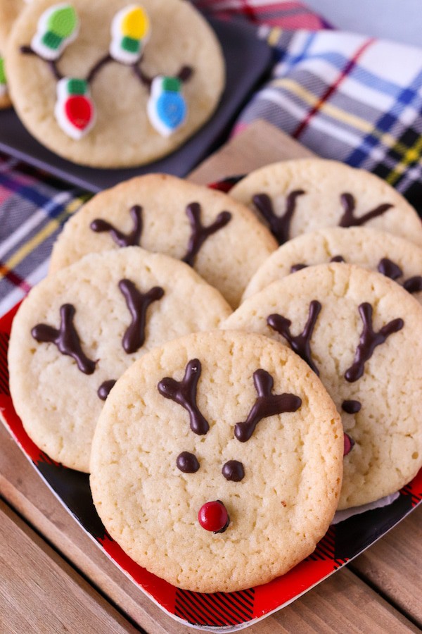 Top view of 6 sugar cookies decorated with Reindeer face and antlers.  In  the back a cookie with christmas lights decoration is visible - Easy Christmas Cookies