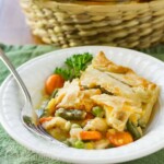 Side view of chicken pot pie in a white bowl with a fork and a green background.