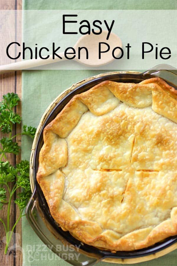 Overhead shot of full chicken pot pie in pan on a green cloth with a wooden spoon and herbs.