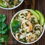 Overhead shot of shrimp in a white bowl with cilantro and lime garnish.