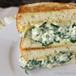 2 artichoke spinach sandwich halves stacked on top of each other on a white plate