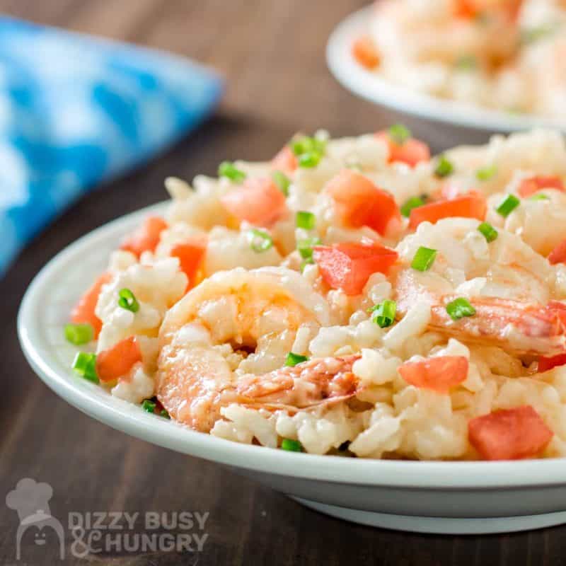 Side shot of creamy rice and shrimp on a white plate on a wooden table with a blue cloth on the side.