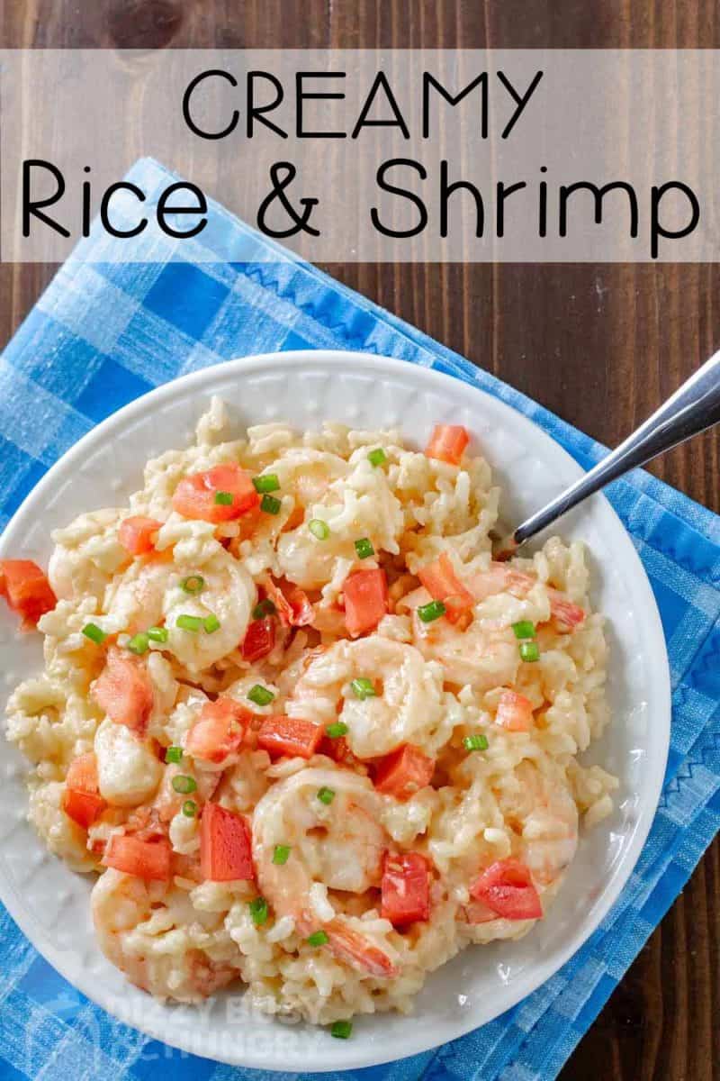 Overhead shot of creamy rice and shrimp on a white bowl with a fork on the side on a blue plaid cloth.