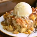 Front view of a slice of Apple Pie Pudding on a white plate, topped with a scoop of vanilla ice cream. A fork is on the plate