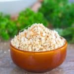 Front view of a small brown bowl filled with bread crumbs. Parsley is blurred in the background