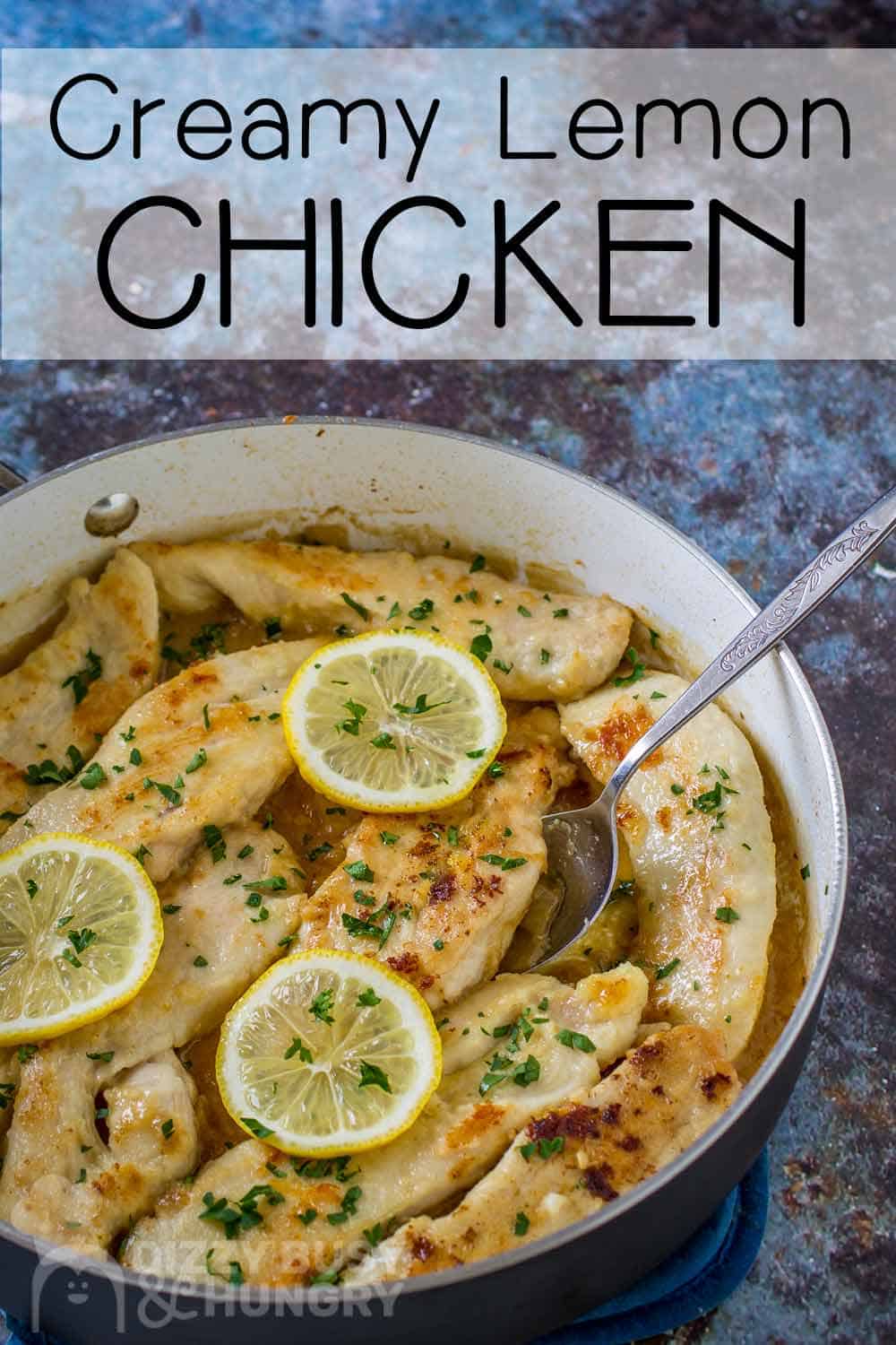 Side shot of creamy lemon chicken in a skillet garnished with lemon slices and herbs with a spoon.