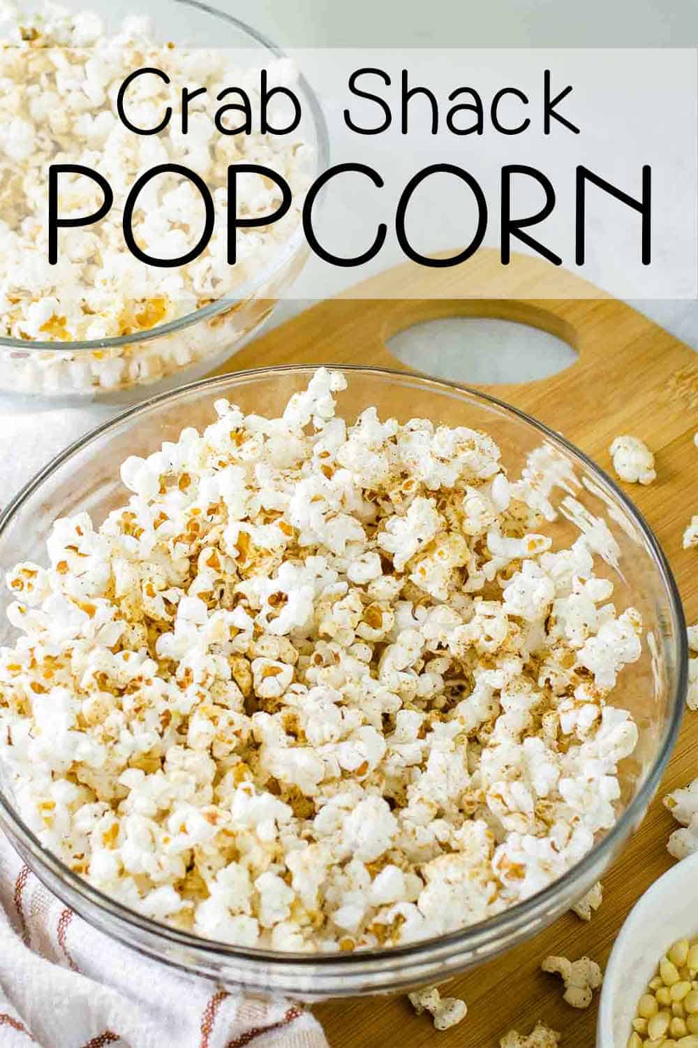 Close up shot of popcorn with homemade seasoning in a clear bowl on a wooden cutting board with popcorn sprinkled around.