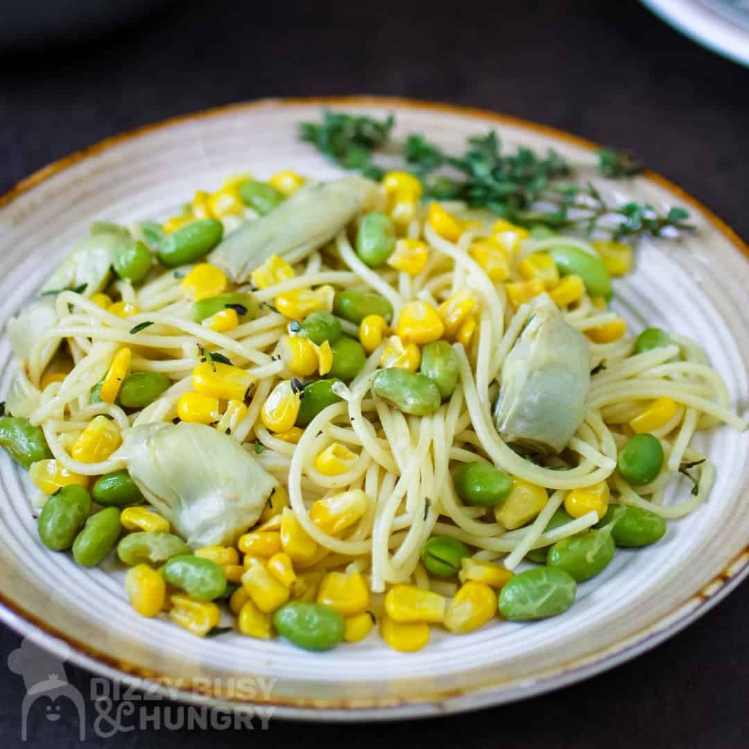 Spaghetti on a plate along with artichoke, corn, edamame, and lemon and thyme.