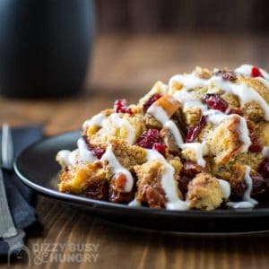 Side view of crock pot French toast casserole on a black plate on a wooden surface with a black napkin and silverware on the side.