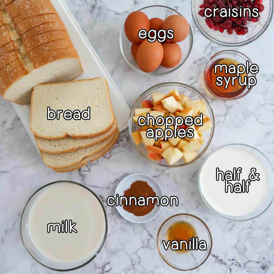 Overhead shot of ingredients- bread, eggs, craisins, maple syrup, chopped apples, milk, cinnamon, vanilla, and half and half.