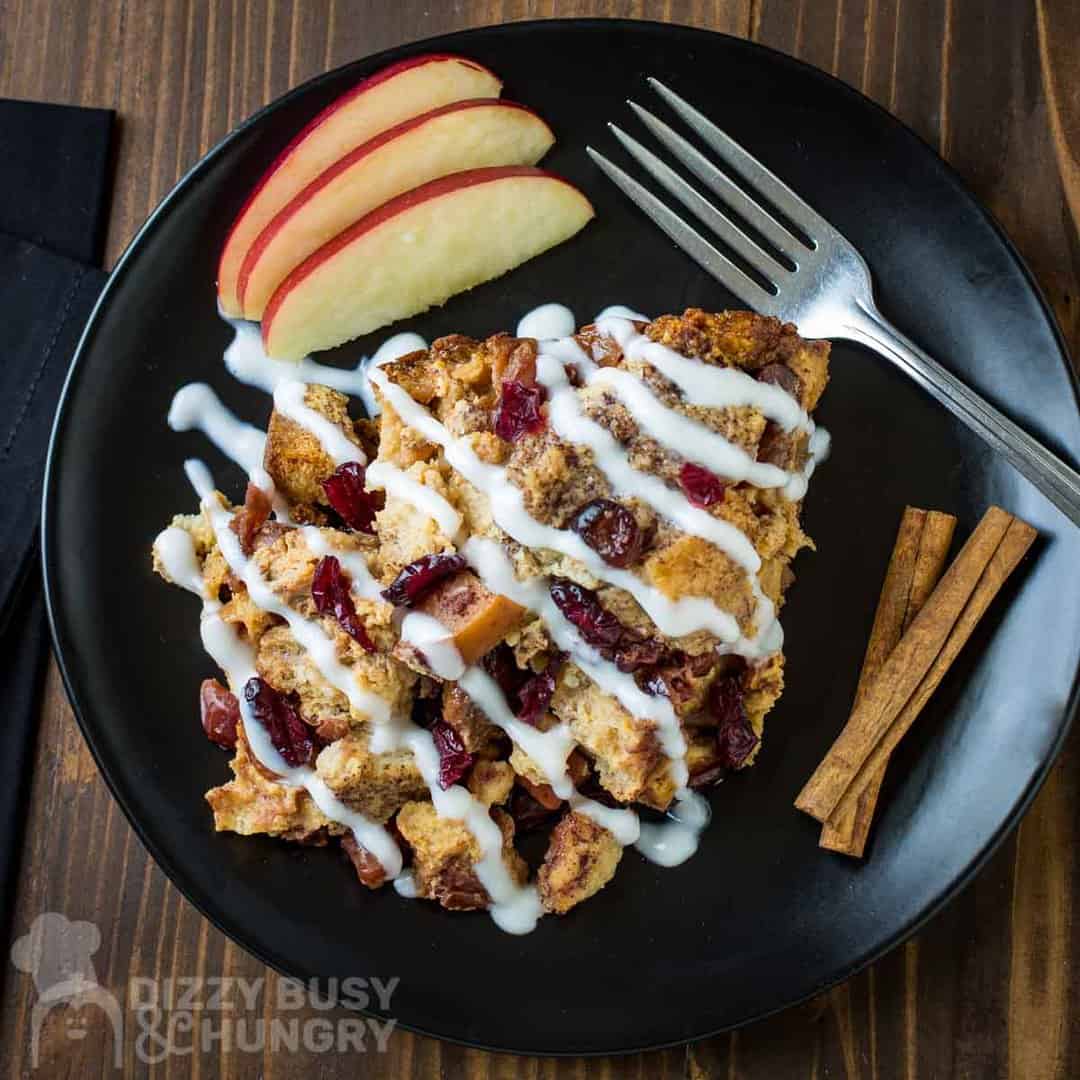 Overhead shot of crock pot French toast casserole on a black plate with a fork, apple slices, and cinnamon sticks on the side.