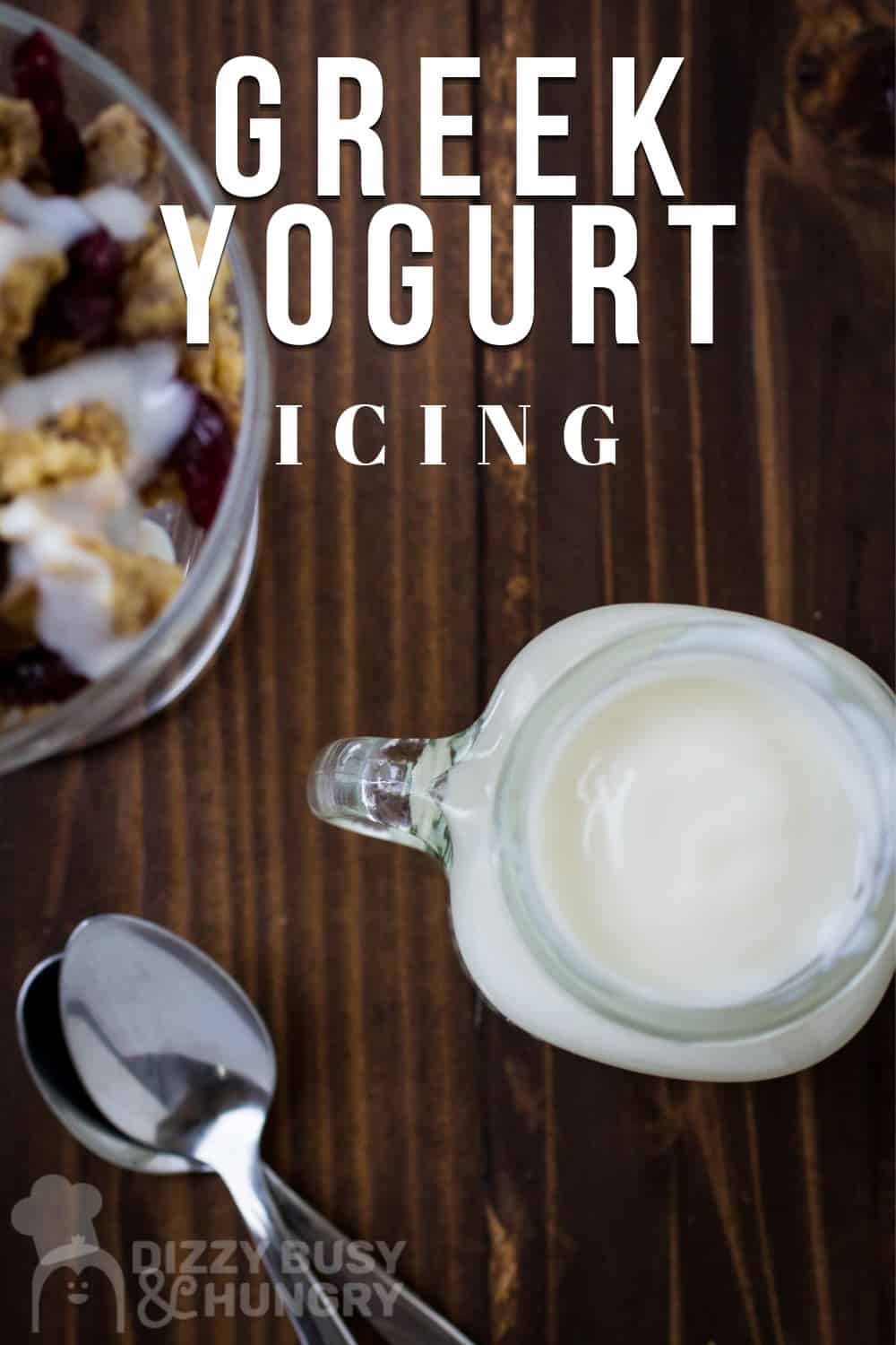 Overhead shot of greek yogurt in a mason jar with a glass and spoons on the side on a wooden surface.