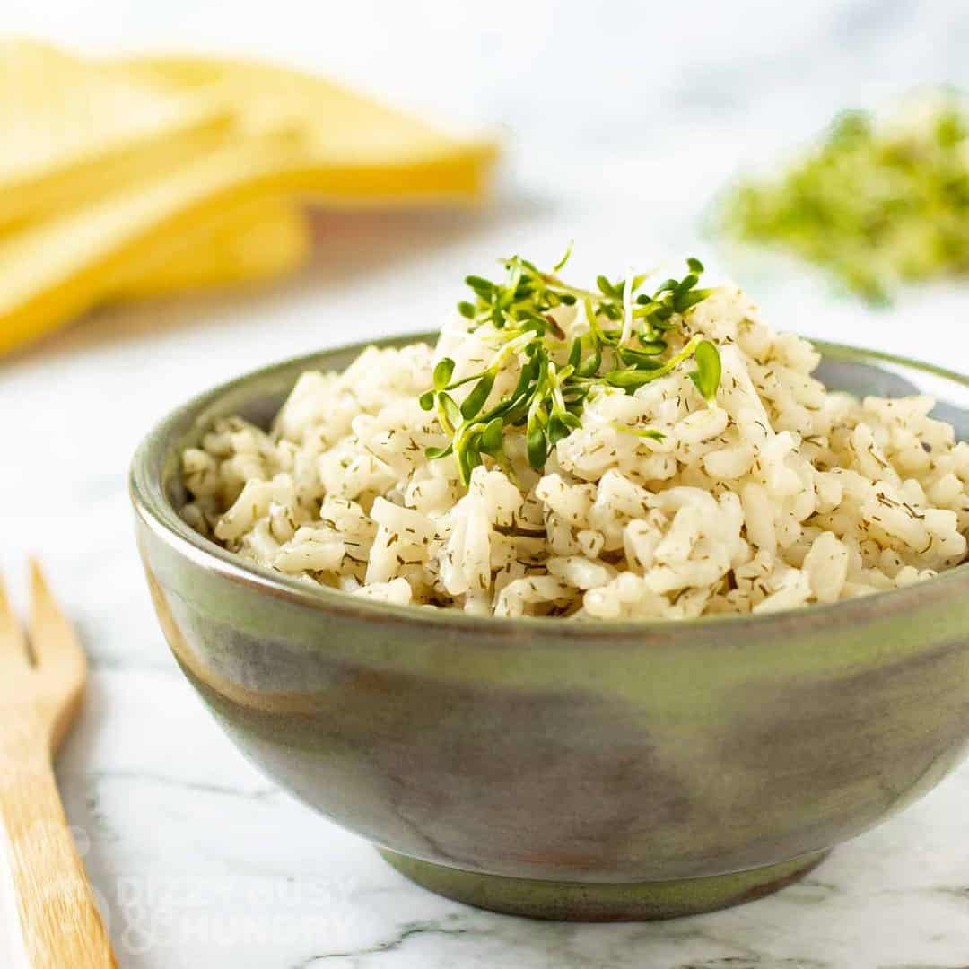 Side view of lemon dill rice garnished with herbs in an olive green bowl on a marble table with a wooden fork on the side.