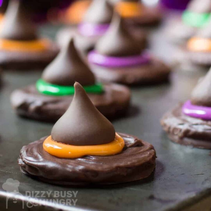 Round chocolate cookie topped with chocolate kiss pressed into orange frosting on a baking sheet.
