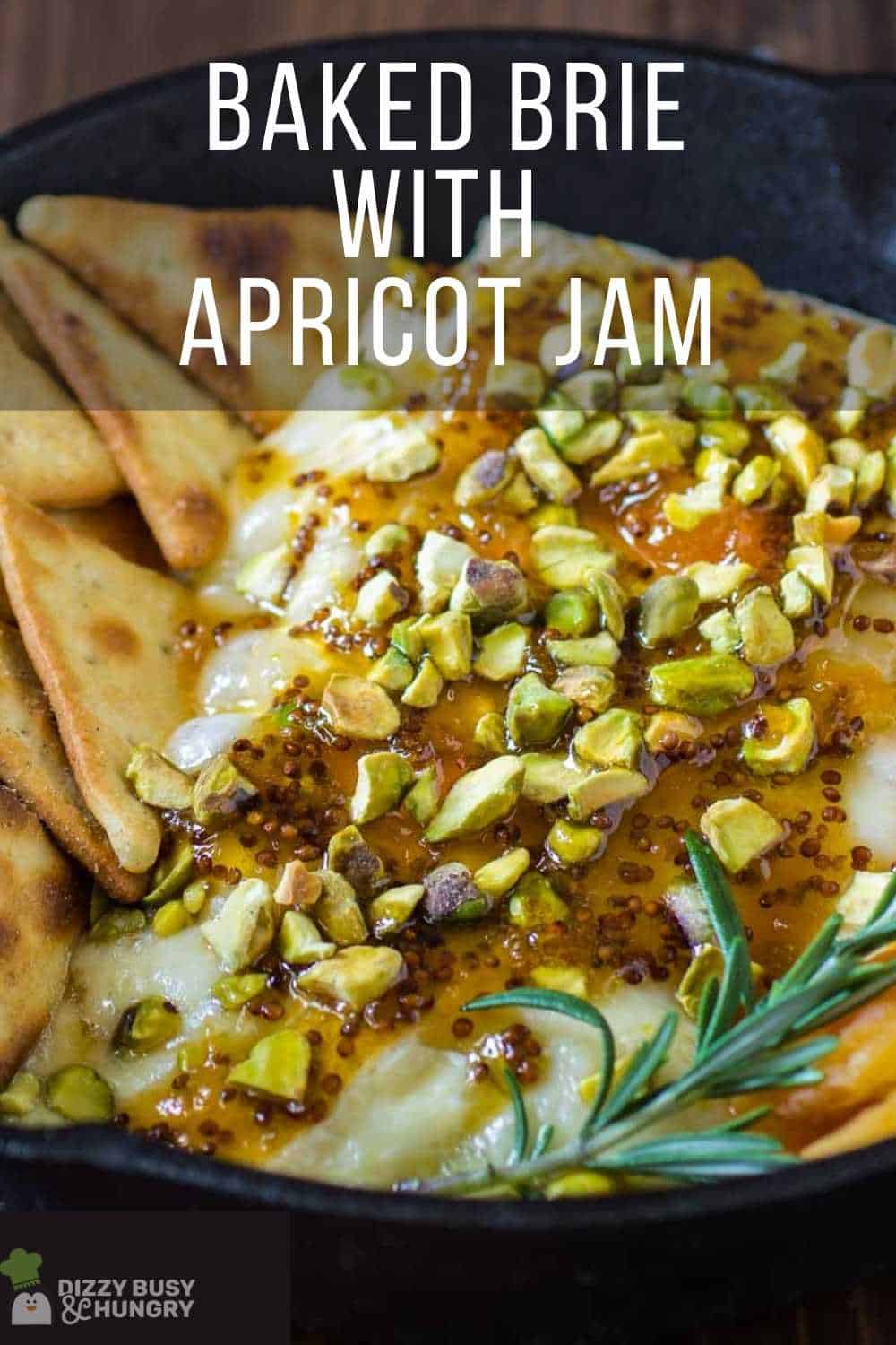 Close up view of baked brie with pita chips, apricots, and herbs in a skillet on a wooden surface.