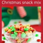 Side view of Christmas snack mix in a white bowl with M&Ms scattered around on a white table, with Christmas decorations in the background.