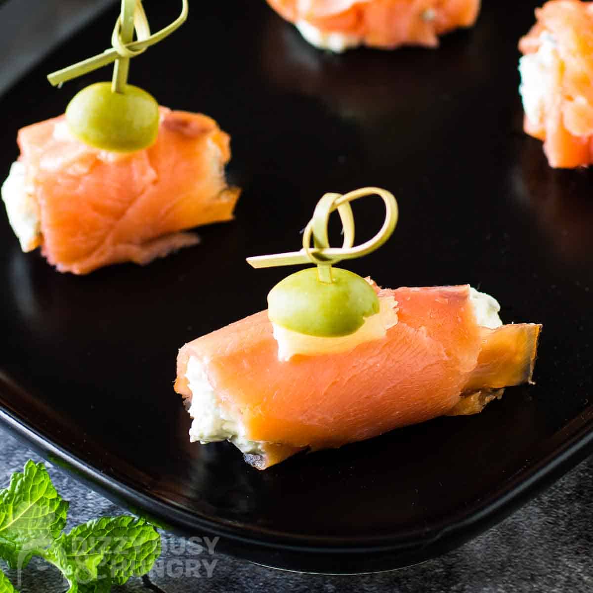 Overhead side view of smoked salmon bites on a black plate with herbs on the side.