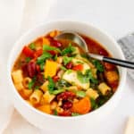 A white bowl with vegetarian minestrone with a spoon inside.